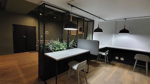 A modern office space with a wooden floor, a white desk, two chairs, a black partition, and pendant lighting. - 15 Sunny 1-bedroom Apartment (Johannesburg)