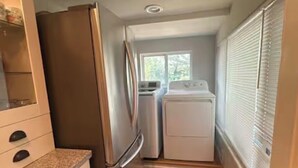 Eine kompakte Küche mit Kühlschrank, Waschmaschine und Trockner, Holzboden und einem Fenster mit Jalousien.