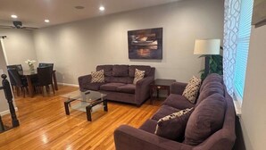 Ein Wohnzimmer mit zwei Sofas, einem Couchtisch, einem Esstisch mit Stühlen und einem Deckenventilator.