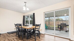 A dining area with a wooden table and chairs, a ceiling light fixture, and a sliding glass door leading to an outdoor patio.