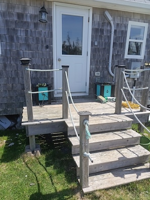 A wooden deck with rope barriers, a white door, and a window with a view of trees.