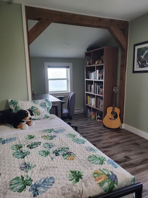 A bedroom with a bed, a desk, a bookshelf, a guitar, and a window.