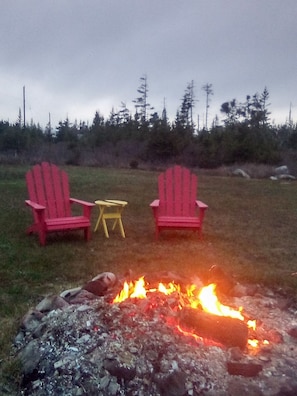 A fire pit with two red chairs and a small yellow table in a grassy outdoor area.