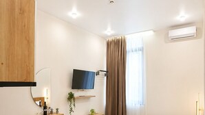 Une chambre d’hôtel moderne avec un bureau en bois, un lit recouvert d’une courtepointe verte, un téléviseur à écran plat fixé au mur et un appareil de climatisation.