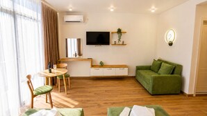 A modern hotel room with a wooden floor, green sofa, a flat-screen TV, a small dining table, and a green massage table. - PARALLEL Apartments (Gonio)