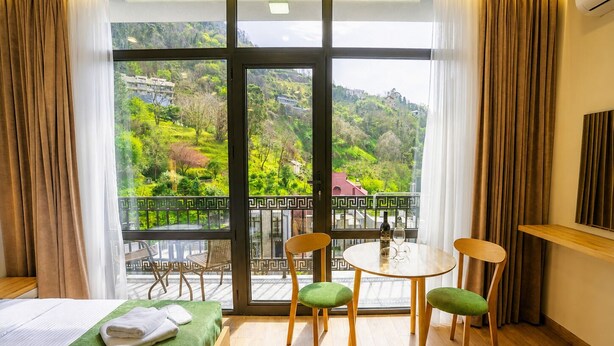 Une chambre d’hôtel avec un balcon, un lit, une table avec des chaises et une vue sur un paysage verdoyant.
