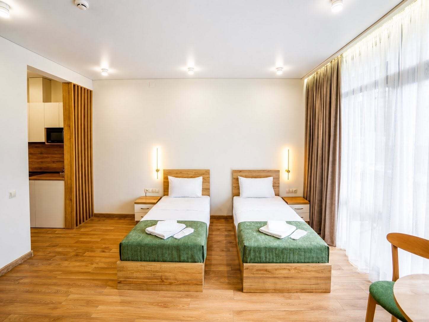 A hotel room with two beds, wooden headboards, bedside tables, a green bench, and a chair.