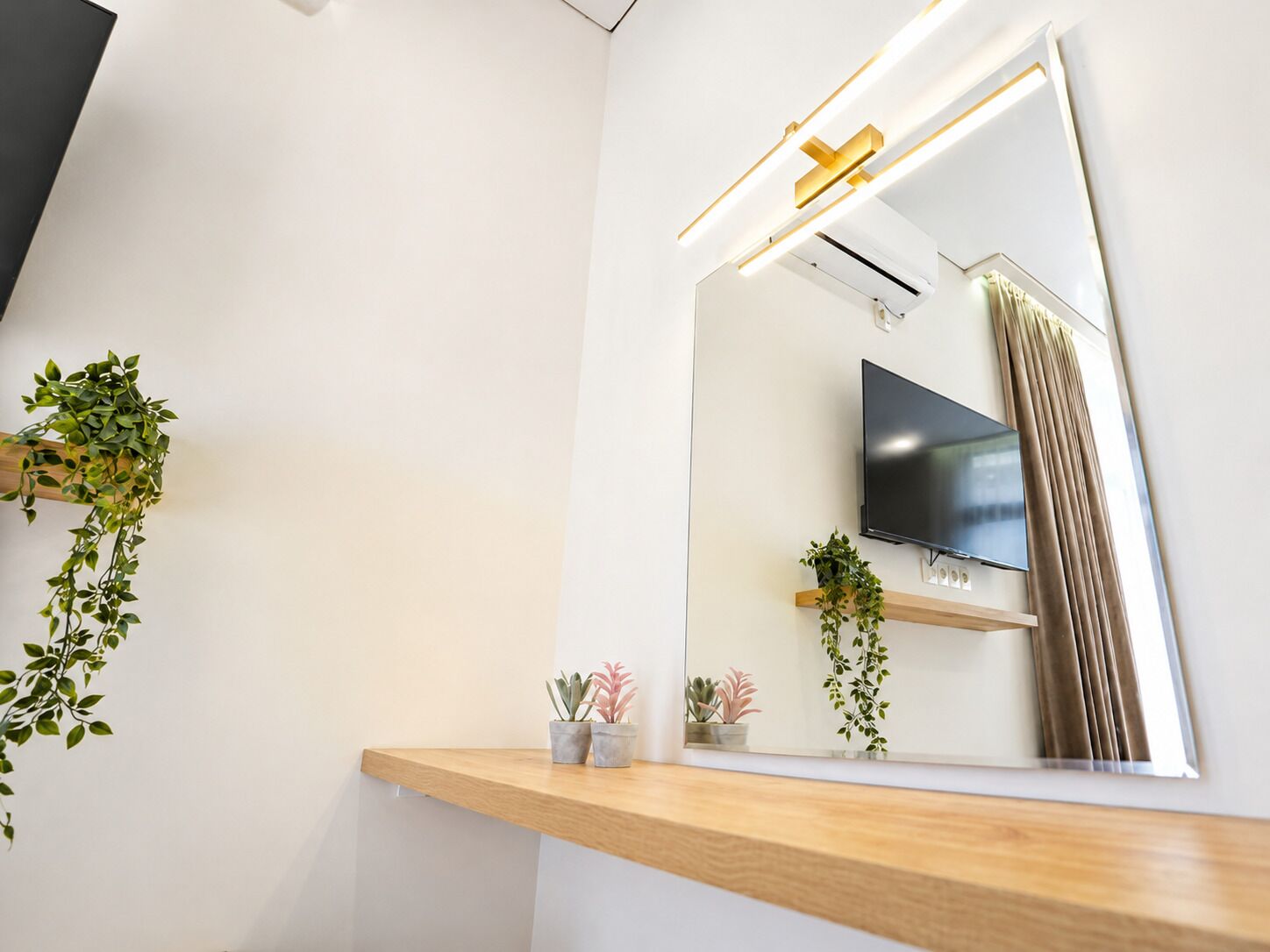 Un baño moderno con un espejo grande, un televisor montado y plantas en macetas.