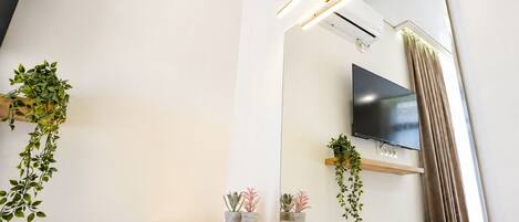 Un baño moderno con un espejo grande, un televisor montado y plantas en macetas.