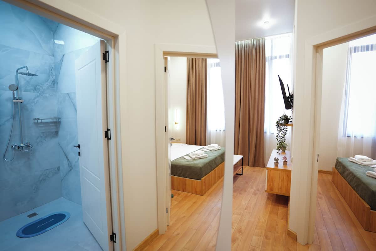 A hotel room with a shower, a bed, a bedside table with a plant, and a bench.