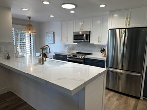 A modern kitchen with white cabinetry, stainless steel appliances, and a marble countertop. - Golf course frontage with stunning mountain views in Ironwood Country club. (Palm Desert)