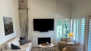 Una sala de estar moderna con un sofá blanco, una mesa de centro redonda y un televisor de pantalla plana montado en una pared blanca.