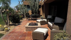 Un patio al aire libre con suelo de baldosas, mobiliario exterior y una variedad de cactus y otras plantas.