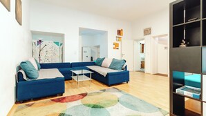 Un salón con un sofá azul, una mesa de centro de vidrio y una alfombra abstracta y colorida.