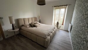 Een slaapkamer met een bed, nachtlampjes, een raam met gordijnen en een hangstoel.