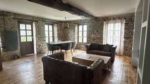 Een kamer met stenen muren, een houten vloer, een bank, een salontafel en een eettafel met stoelen.