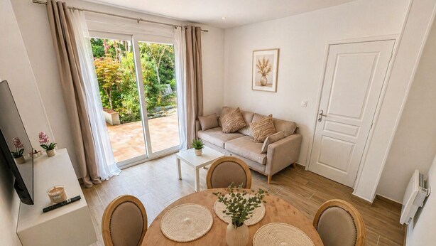 A modern living room with a sofa, a dining table with placemats, a TV on a stand, and a sliding glass door leading to a garden. - ⭐ 70m² with Terrace - Near Paris, CDG & RER B (5min) (Sevran)