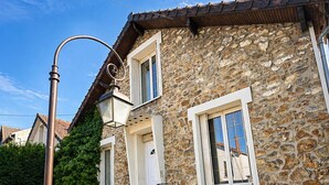 A stone building with a tiled roof, a staircase leading to the entrance, and a street lamp. - ⭐ 70m² with Terrace - Near Paris, CDG & RER B (5min) (Sevran)