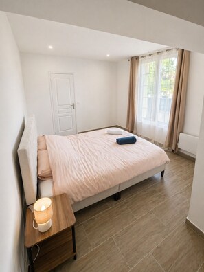 A bedroom with a bed, bedside table, and a window with curtains. - ⭐ 70m² with Terrace - Near Paris, CDG & RER B (5min) (Sevran)