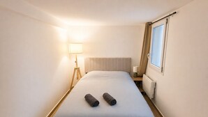 Quarto de hotel com cama, luminária, janela com cortinas e radiador.