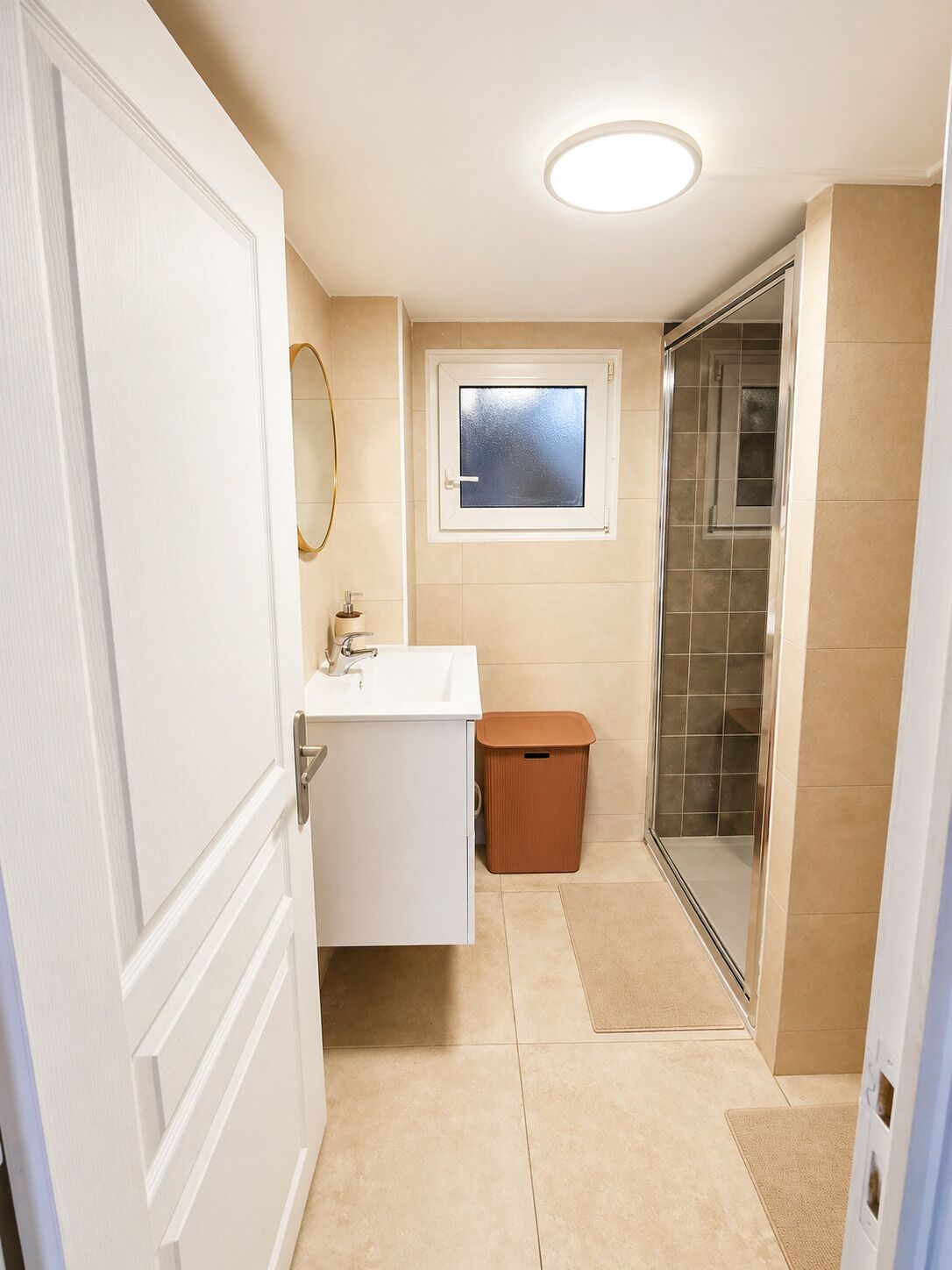 Une salle de bain avec un lavabo blanc, un miroir, une fenêtre et une douche.