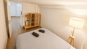 Quarto com cama, guarda-roupa de madeira, abajur e porta para outro cômodo.
