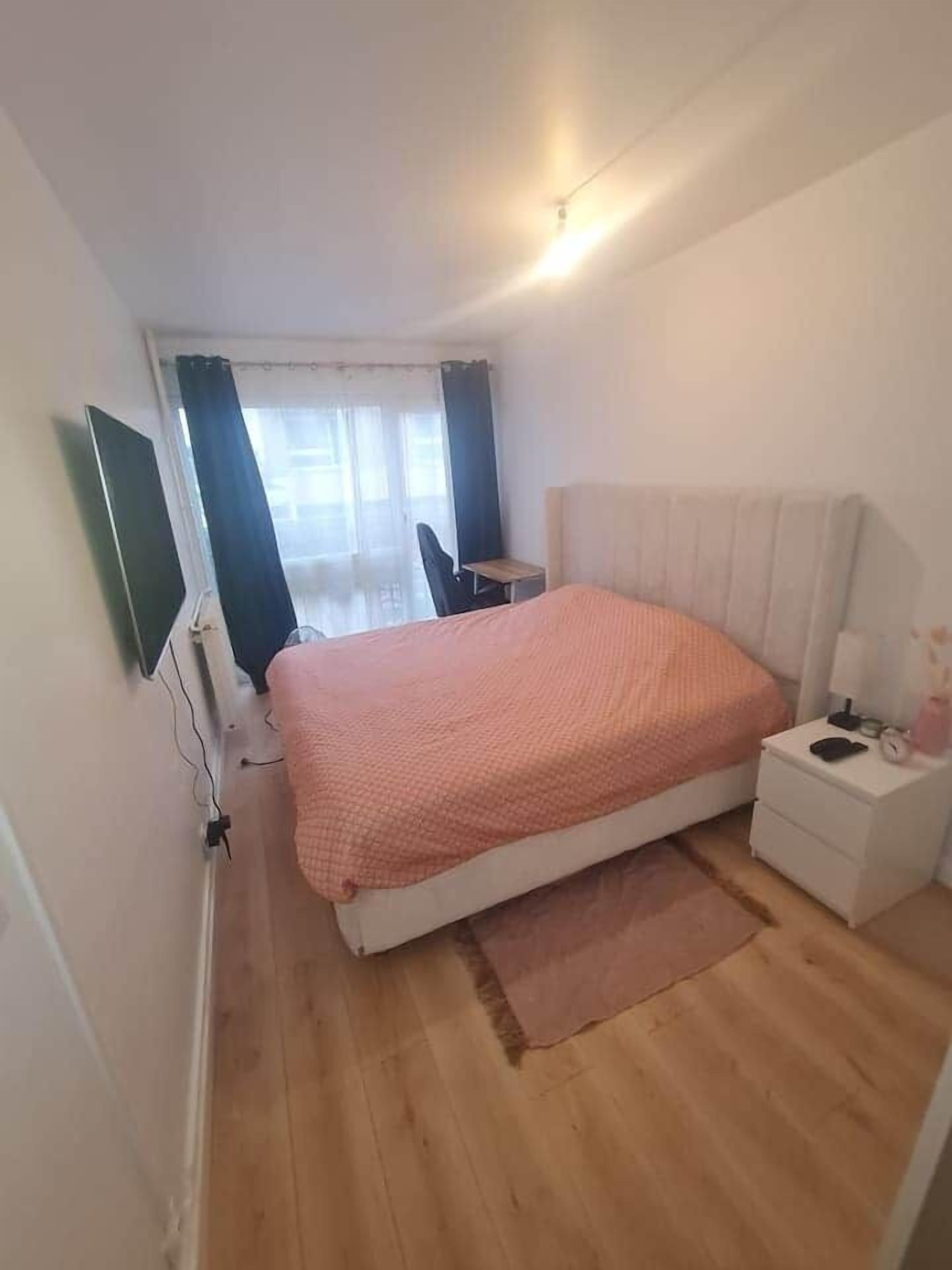 Quarto com cama, mesa de cabeceira e televisão fixada na parede.