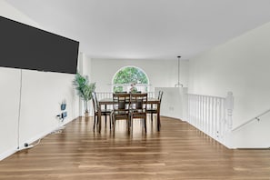 Ein geräumiges Zimmer mit Esstisch, Stühlen, einem großen Fenster und einer Treppe.