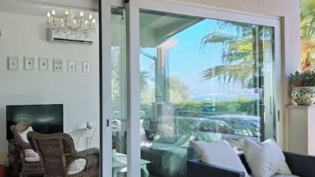 Un salon moderne avec une porte vitrée donnant sur un balcon, des meubles en osier et un téléviseur à écran plat.