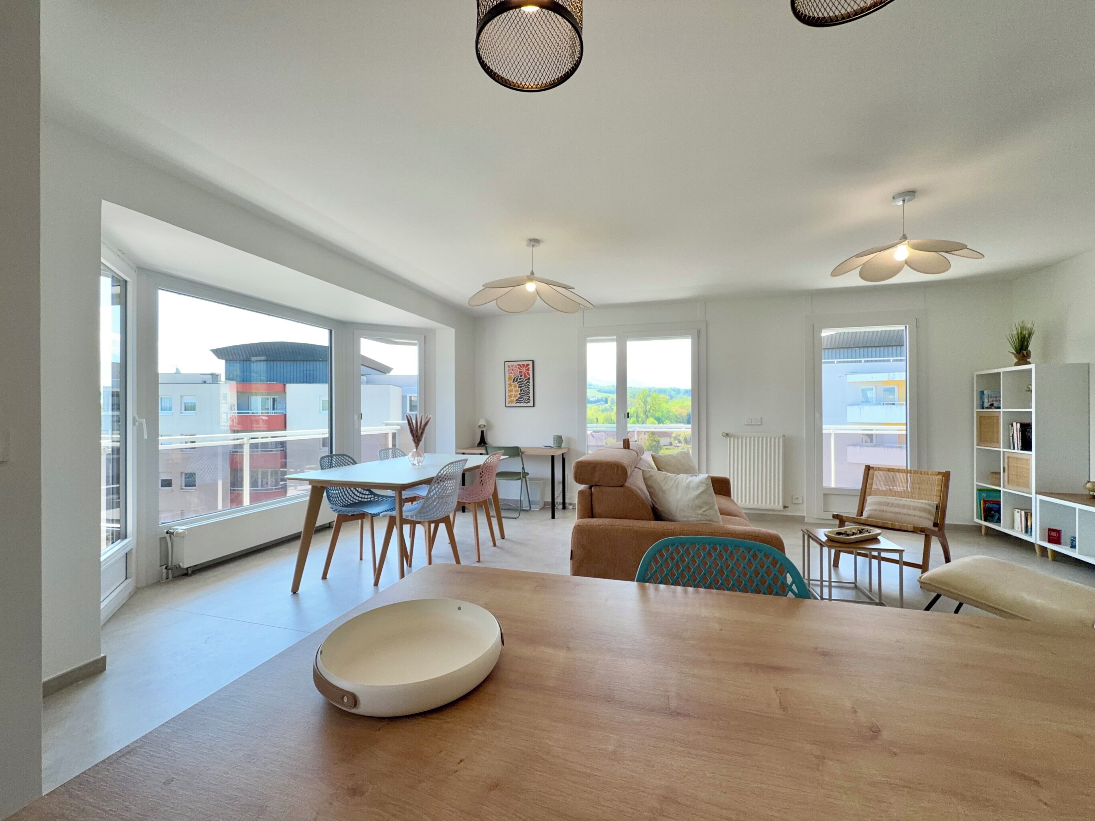 A modern living room with a dining area, large windows, and a view of buildings.