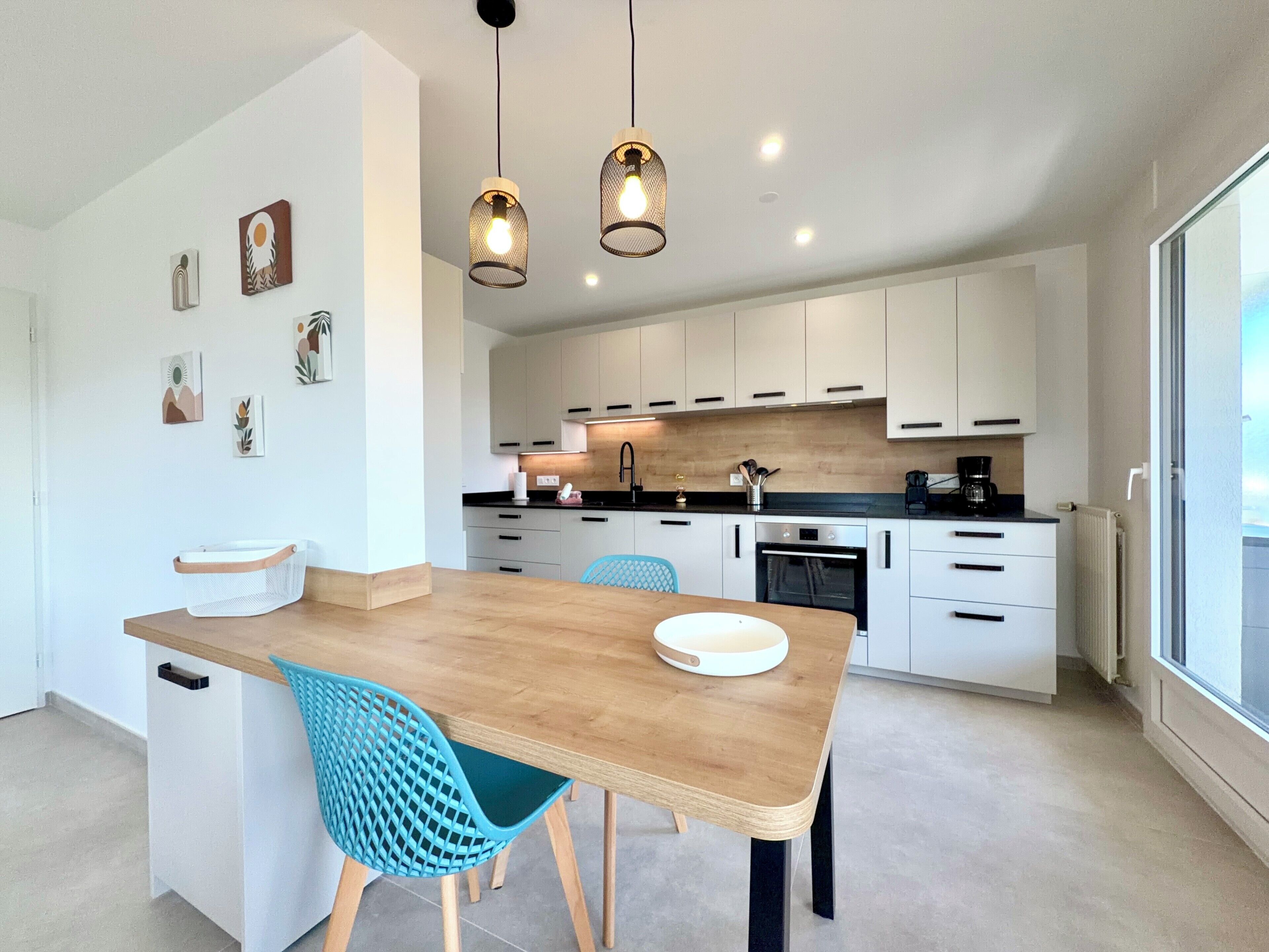 A modern kitchen with white cabinets, a wooden dining table, and blue chairs.