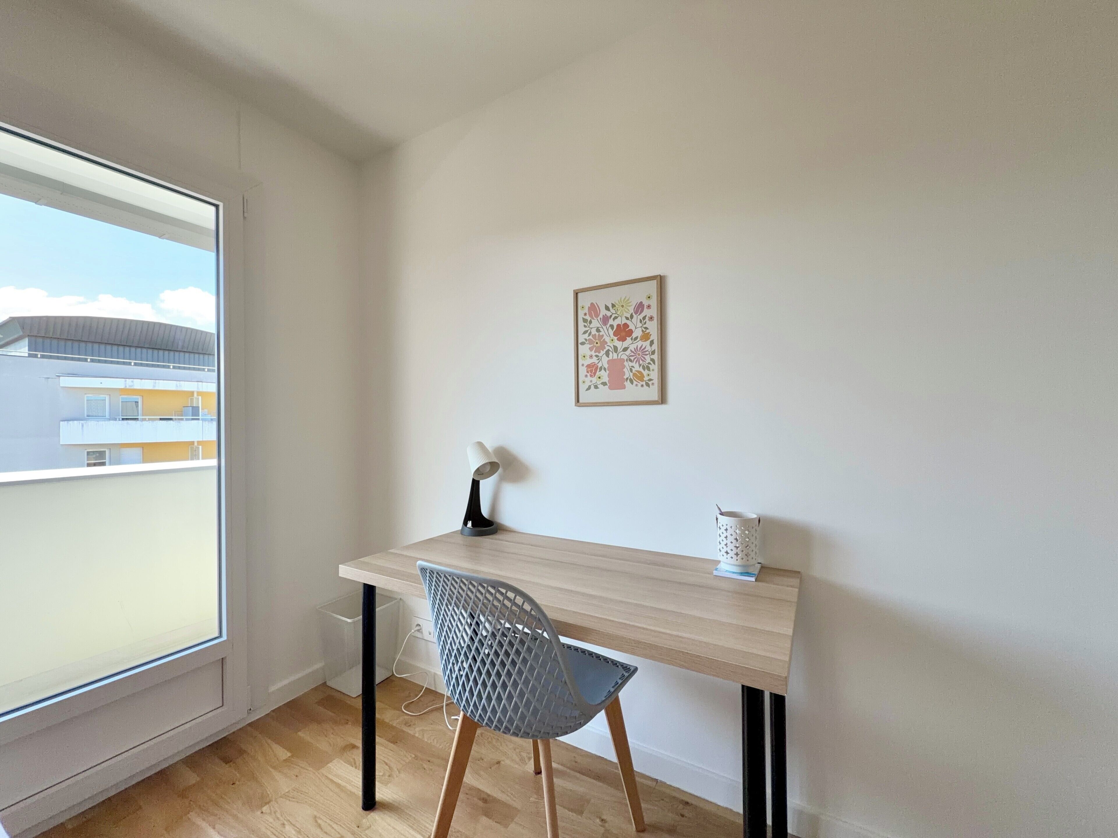 A room with a desk, chair, window, and a framed picture on the wall.