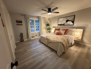 A bedroom with a bed, a ceiling fan, a window with curtains, a bedside table with a lamp, and a wall-mounted artwork. - Delightful 3-bedroom house with AC in charming Buford (Buford)
