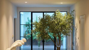 Un couloir orné d’un grand arbre en pot, d’une sculpture et offrant une vue à travers une porte vitrée.