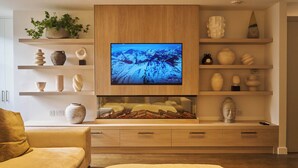 Un salon moderne doté d’un téléviseur à écran plat, d’étagères en bois ornées d’objets décoratifs, d’un canapé et d’une cheminée.