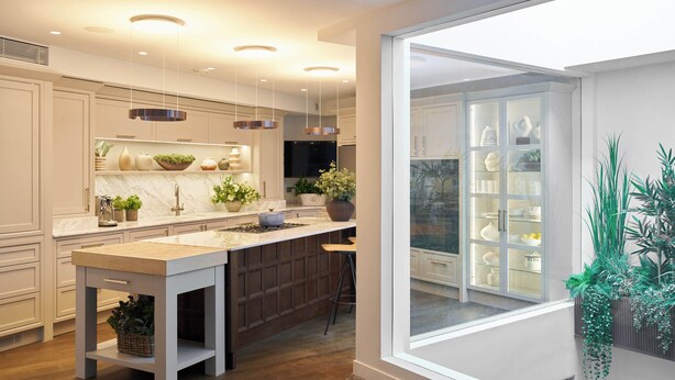 Une cuisine moderne dotée d’un grand îlot central, de luminaires suspendus et offrant une vue dégagée grâce à une grande fenêtre.