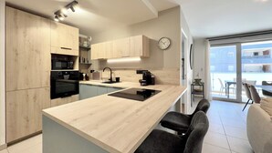 A modern kitchen with a central island, built-in appliances, and a view to a balcony. - T4 5 personnes à 300m du Lac (Aix-les-Bains)