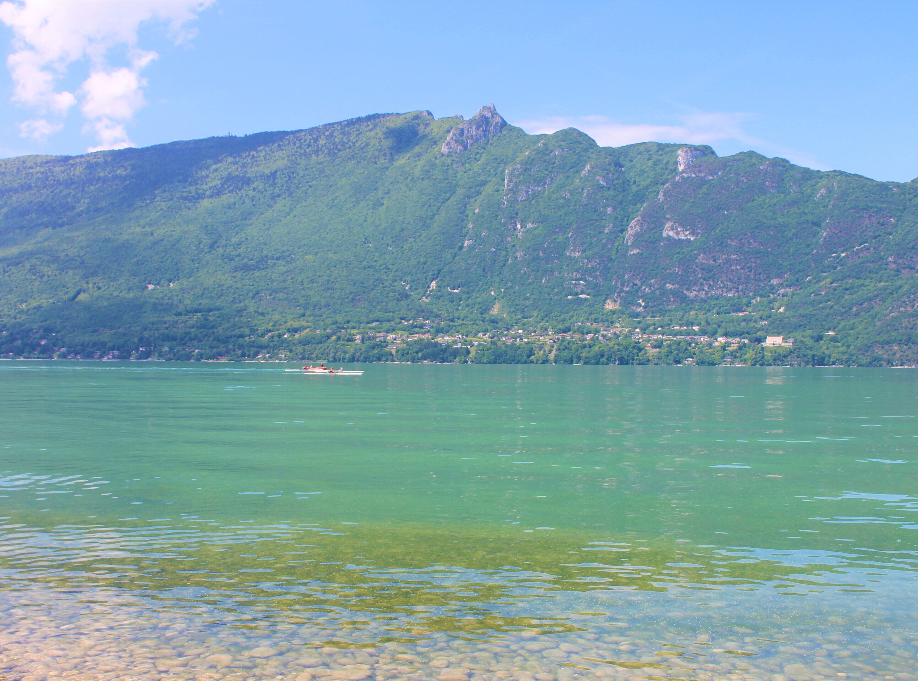 Un lago con un bote, agua cristalina y una montaña al fondo.