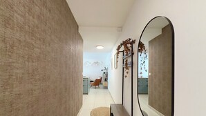 A hallway with a textured wall, a round mirror, a bench, and a view of a dining area with a mountain mural. - T4 5 personnes à 300m du Lac (Aix-les-Bains)