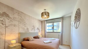 A bedroom with a bed, bedside tables, a lamp, a window, and a wall with a tree mural. - T4 5 personnes à 300m du Lac (Aix-les-Bains)