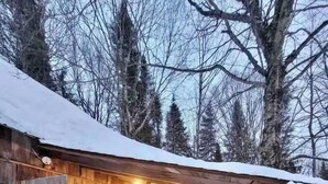 A wooden cabin with a snow-covered roof, a bench, and string lights. - Authentic Ranch Experience Close to Mont-Tremblant (Val-des-Lacs)
