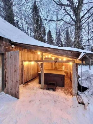 A wooden cabin with a snow-covered roof, a bench, and string lights. - Authentic Ranch Experience Close to Mont-Tremblant (Val-des-Lacs)