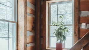 A cabin interior with wooden walls, a window with a plant, and a wooden staircase. - Authentic Ranch Experience Close to Mont-Tremblant (Val-des-Lacs)
