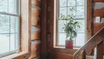 A cabin interior with wooden walls, a window with a plant, and a wooden staircase.