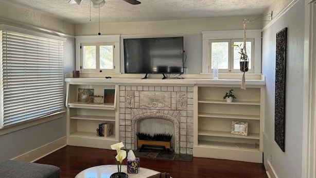 A living room with a fireplace, television, and ceiling fan.