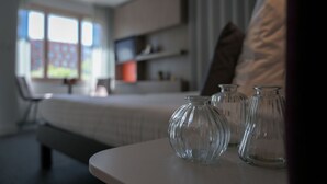 Moderni huone, jossa on sänky, lasivaaseilla koristeltu pöytä ja ikkuna, jossa on sälekaihtimet.