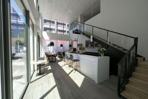 A modern kitchen with a central island, a dining area with chairs, and a staircase with glass railings. - Moderne studio au centre de Lyon | Piscine + Wi-Fi (Lyon)