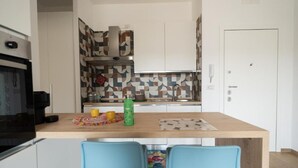 Een compacte keuken met een centraal eiland, twee blauwe stoelen, een decoratieve spatwand en witte kastjes.