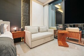 Ein modernes Hotelzimmer mit einem Bett, einer Couch, einem Holznachttisch, einem kleinen Tisch und einem großen Fenster mit Blick.
