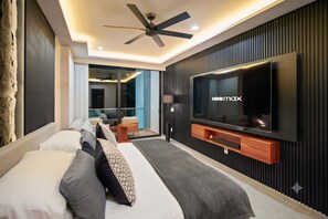 Ein modernes Hotelzimmer mit einem großen Bett, einem an der Wand montierten Fernseher, einem Deckenventilator und Blick auf die beleuchtete Stadt bei Nacht.